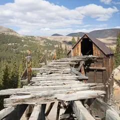 An abandoned mine sits in the middle of a mountainous forest, its wooden structure weathered and worn from years of exposure to the elements.