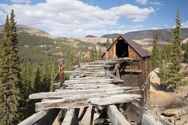 An abandoned mine sits in the middle of a mountainous forest, its wooden structure weathered and worn from years of exposure to the elements.
