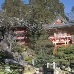 An ornate red pagoda stands among trees and greenery, with multiple levels featuring windows and railings.