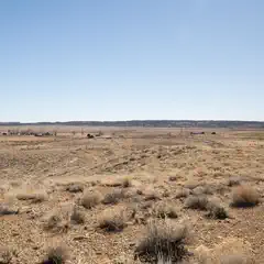 A desert landscape stretches out under a clear blue sky, with a few small buildings scattered across the horizon.