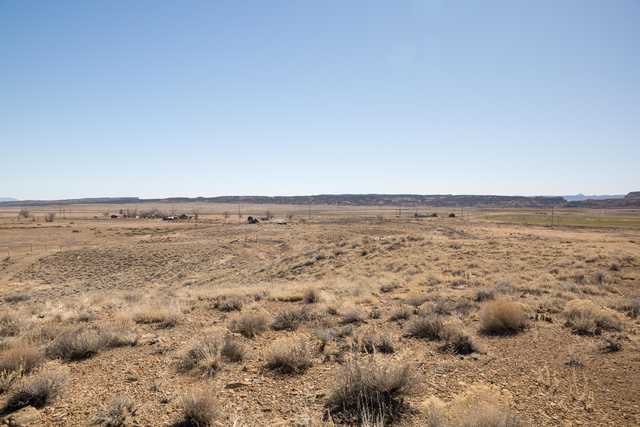 A desert landscape stretches out under a clear blue sky, with a few small buildings scattered across the horizon.