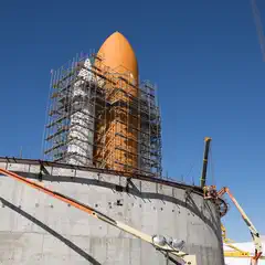 An orange and white rocket on a concrete structure, surrounded by construction equipment.