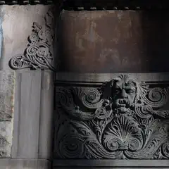 A stone facade features a carved grotesque face with swirling acanthus leaves and ornate scrollwork beneath a shadowed cornice.