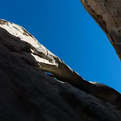 A narrow canyon with tall rock walls that open up to a blue sky above.