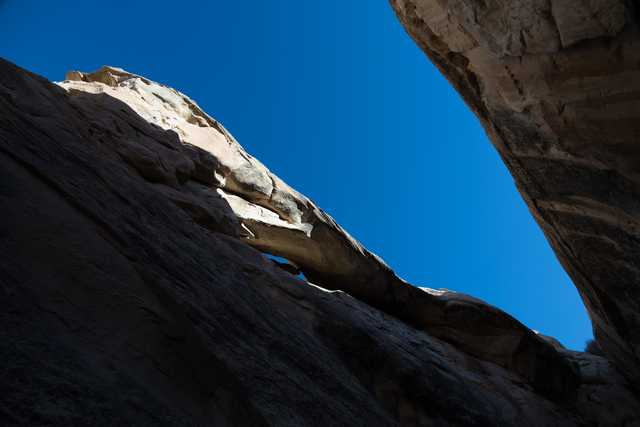 A narrow canyon with tall rock walls that open up to a blue sky above.