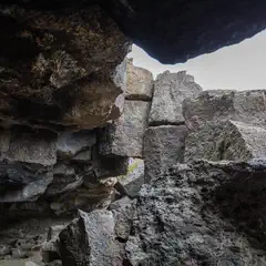 A dark cave opening frames a pile of gray rocks against a cloudy sky.