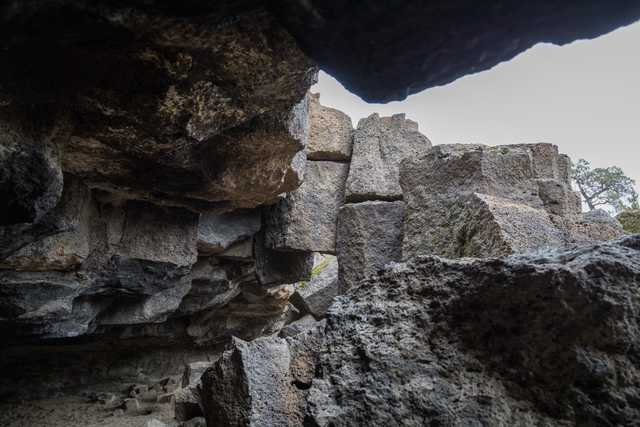 A dark cave opening frames a pile of gray rocks against a cloudy sky.