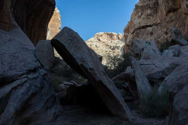 A narrow canyon with tall, jagged rock walls and a clear blue sky above.