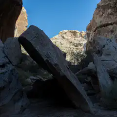 A narrow canyon with tall, jagged rock walls and a clear blue sky above.