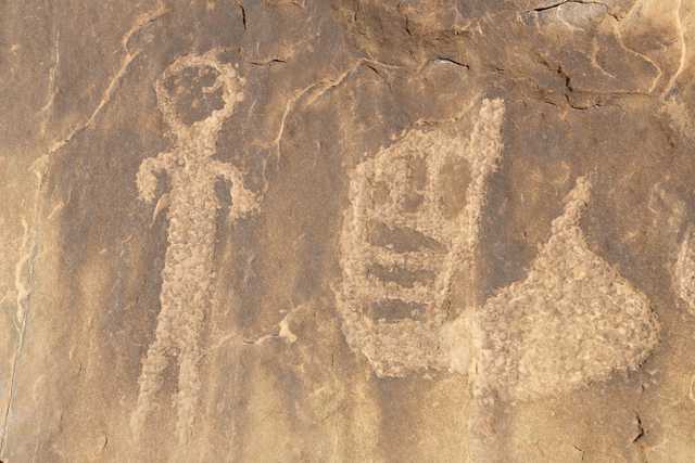 A rock surface with petroglyphs of a human figure and various other shapes.