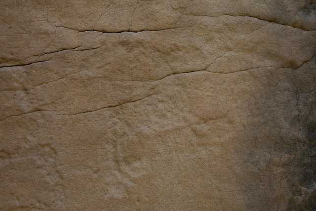 A beige rock face with prominent horizontal cracks and lines under faint petroglyphs of animals.