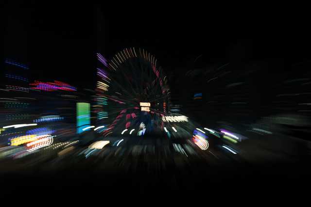 A nighttime zoom burst captures a brightly lit Ferris wheel and surrounding amusement park lights as streaks radiating from the center.