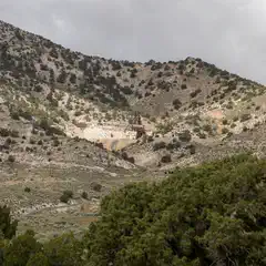 A rugged hillside with sparse vegetation and a small open-pit mine.