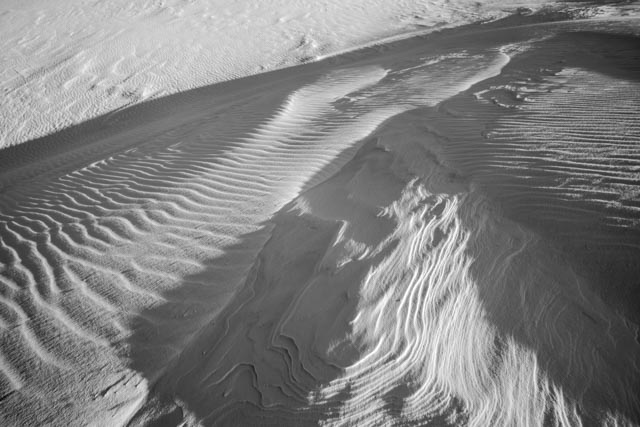 An expanse of white sand is covered with intricate patterns of ripples and ridges.