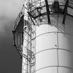 A cylindrical metal tank has a spiral staircase attached to its exterior and a caged platform extending from the side.