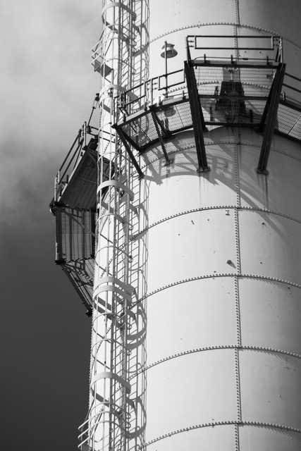 A cylindrical metal tank has a spiral staircase attached to its exterior and a caged platform extending from the side.