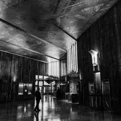 A lone figure walks through a grand, dimly lit lobby with polished marble walls, illuminated columns, and a detailed ceiling mural.