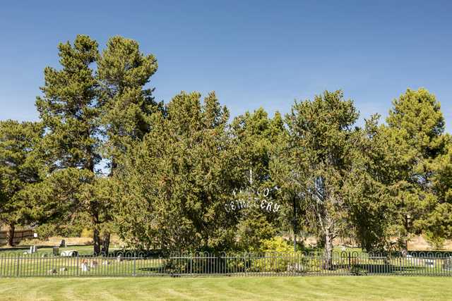 An iron fence surrounds a cemetery, with a sign reading 'Frisco Cemetery' partially obscured by trees.