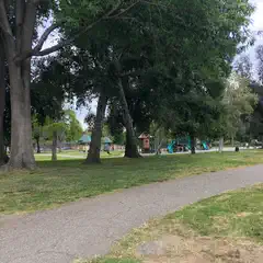 A path leading through a park, lined by trees and a playground.