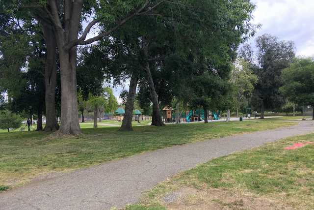 A path leading through a park, lined by trees and a playground.