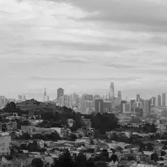 A densely packed urban landscape with numerous buildings and hills in the foreground and a skyline of tall buildings in the background.