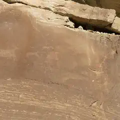 A sandstone cliff face features a large petroglyph of an animal, possibly a bison or deer.