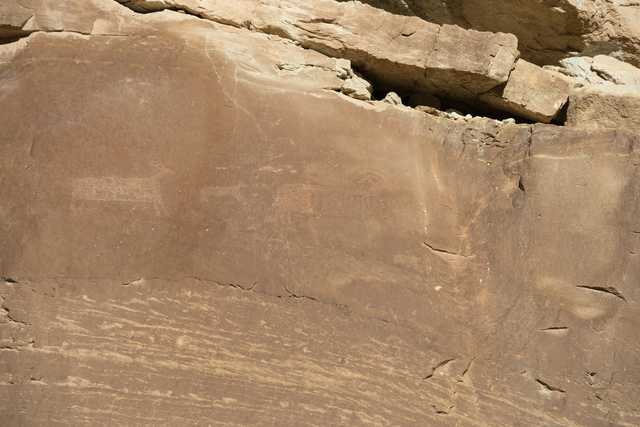A sandstone cliff face features a large petroglyph of an animal, possibly a bison or deer.