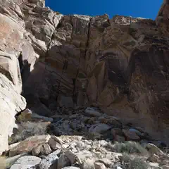 A large rocky cliff is visible from below, rising up to meet a clear blue sky.