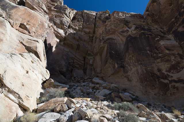 A large rocky cliff is visible from below, rising up to meet a clear blue sky.