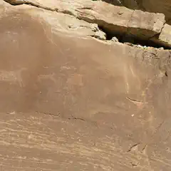 A sandstone cliff face features a large petroglyph of an animal, possibly a bison or deer.