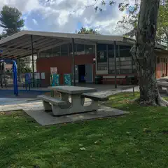 A brick building with a sloped roof stands behind outdoor play equipment including a blue jungle gym.