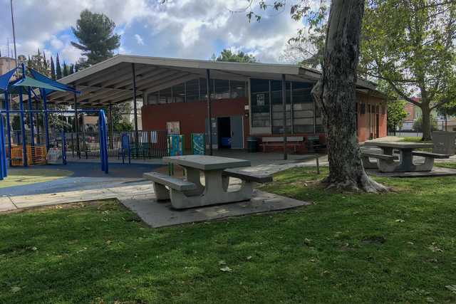 A brick building with a sloped roof stands behind outdoor play equipment including a blue jungle gym.