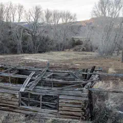 An old wooden cabin is seen from the side, with a fallen roof, and a small window visible on the front wall.