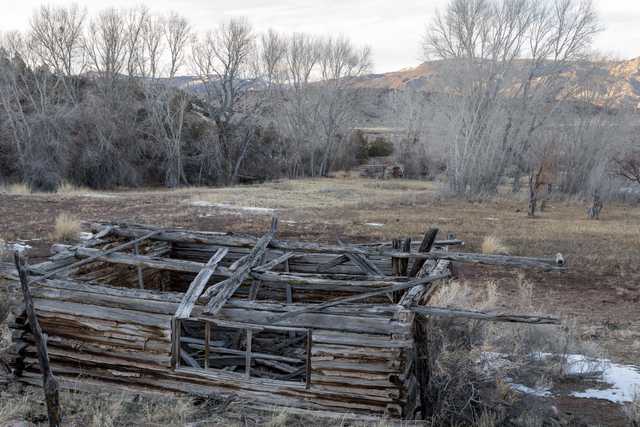 An old wooden cabin is seen from the side, with a fallen roof, and a small window visible on the front wall.