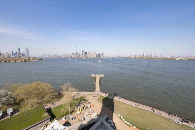 A large body of water with boats and a city skyline in the distance, viewed from an elevated perspective on a clear day.