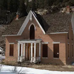 An abandoned red-brick house has boarded-up windows and a white porch with a railing.