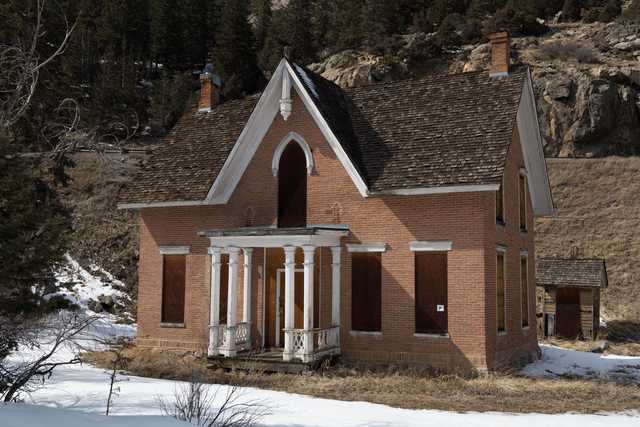 An abandoned red-brick house has boarded-up windows and a white porch with a railing.
