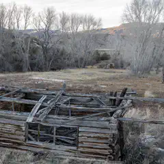 An old wooden cabin is seen from the side, with a fallen roof, and a small window visible on the front wall.