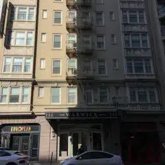 A beige hotel building with fire escapes on the facade, half in the light and half in shadow.