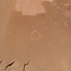 A reddish-orange cliff face features a prominent circular marking in its center.