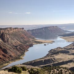 A winding river flowing through a rugged landscape with red rock formations and sparse vegetation under a clear sky.