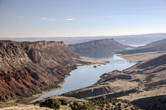 A winding river flowing through a rugged landscape with red rock formations and sparse vegetation under a clear sky.