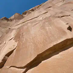 A close-up view of a rocky cliff face with visible cracks and crevices, set against a clear blue sky.