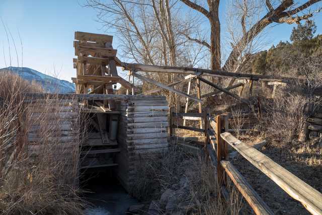 An old wooden water wheel stands beside a small stream, with a wooden trough attached to its edge.