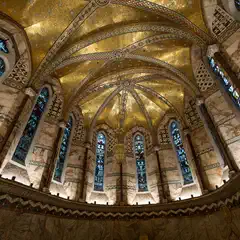 A vaulted interior with a gilded, star-patterned ceiling, arched stained-glass windows, and marble columns with decorative inlays.
