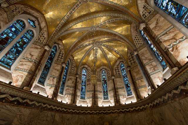 A vaulted interior with a gilded, star-patterned ceiling, arched stained-glass windows, and marble columns with decorative inlays.