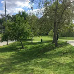 A grassy area features trees, a paved path, and a playground with red slides.