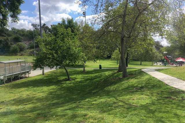 A grassy area features trees, a paved path, and a playground with red slides.