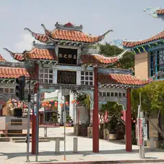 An ornate gate features Chinese characters on a black sign, topped with curved red-tiled roofs and supported by red pillars.