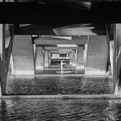 A person is paddleboarding under a concrete bridge with multiple supporting beams.